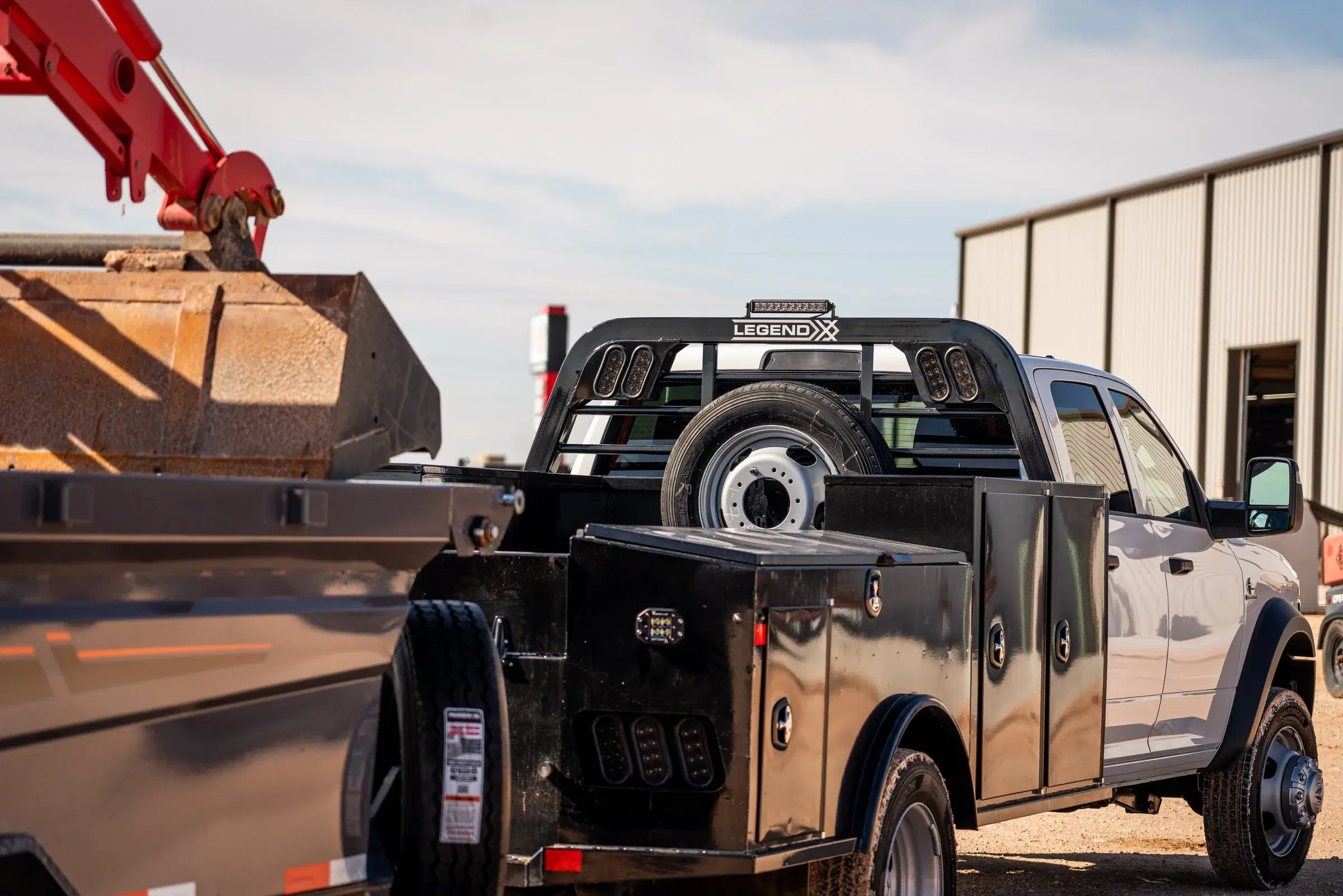 Black Legend X Apollo service body with enclosed toolboxes and a spare tire on a white work truck beside construction equipment